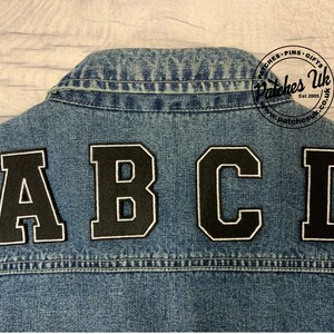 May include: Black felt letters A, B, C, and D sewn onto a blue denim jacket. The letters are in a large, bold font style.