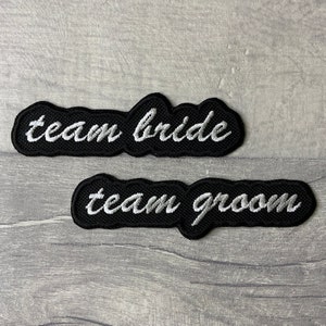 May include: Two black fabric patches with white embroidered text. The top patch says "team bride" and the bottom patch says "team groom".