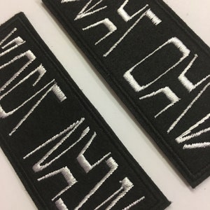 May include: Two black fabric patches with white embroidered text. The top patch says "WAR" and the bottom patch says "NEVER"