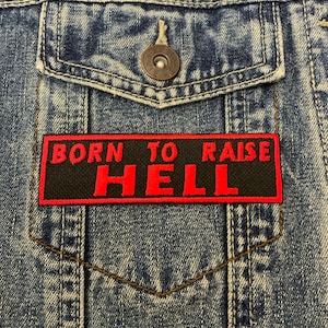 May include: A black and red embroidered patch with the text "Born to Raise Hell" on a denim jacket.