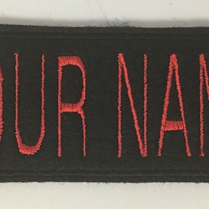 May include: Black fabric patch with red embroidered text that reads "YOUR NAME".