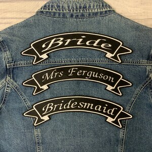 May include: Three black and white fabric patches with white text on a denim jacket. The top patch says "Bride", the middle patch says "Mrs. Ferguson", and the bottom patch says "Bridesmaid".