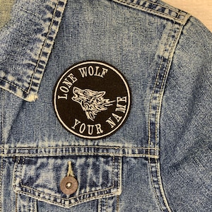 May include: A black and white embroidered patch with a howling wolf and the text "Lone Wolf Your Name" on a denim jacket.