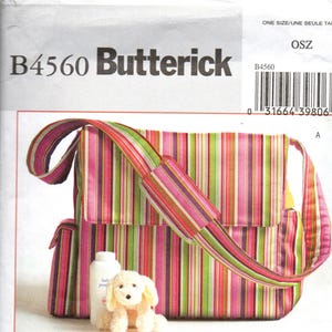 May include: A Butterick B4560 sewing pattern envelope featuring a multi-colored striped messenger bag with a flap closure and shoulder strap. The image includes a small white plush dog toy and a white bottle in front of the bag.