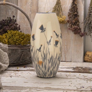 Op de afbeelding: Een crèmekleurige keramische vaas met een hoge, ovale vorm. De vaas is versierd met een handgeschilderd ontwerp van zwarte en oranje wilde bloemen.