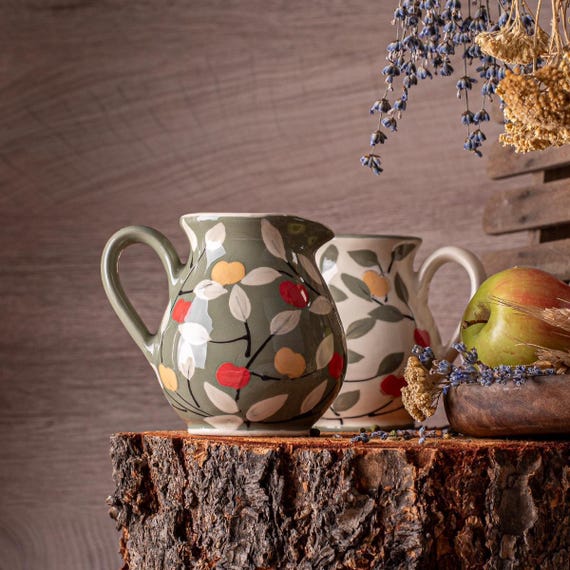 Hand-thrown ceramic apple jug with green and white glaze — the kind of one-of-a-kind farmhouse pottery piece you'd spot on a design blog and immediately want on your shelf.
