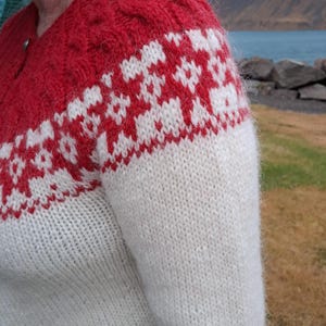 May include: A red and white knitted sweater with a cable knit pattern on the shoulders and a geometric pattern on the sleeves.