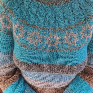 May include: A teal blue knitted sweater with brown, gray, and white stripes. The sweater has a cable knit pattern around the neck.