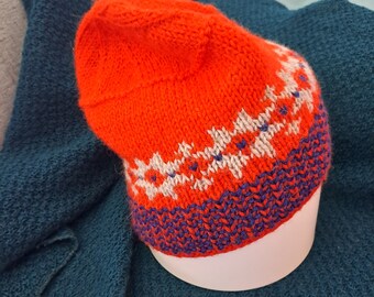 May include: A red knitted hat with a white and blue geometric pattern. The hat has a folded brim and is made of a soft, warm yarn.