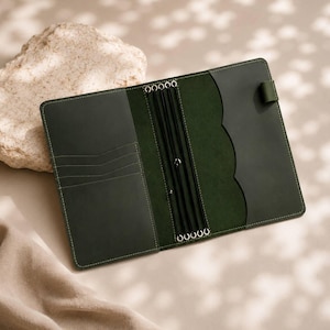 May include: A dark green leather notebook cover featuring an open interior with multiple card slots on the left side, a central spine with four black elastic bands for securing inserts, and a scalloped pocket flap on the right side.