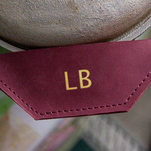 Op de afbeelding: Een bordeauxrood lederen label met de initialen "LB" geborduurd in gouden draad.