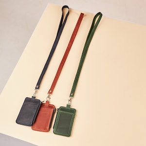 Puede incluir: Tres carteras de identificación de cuero con cordones. Las carteras son de color azul marino, marrón y verde. Cada cartera tiene una cremallera.