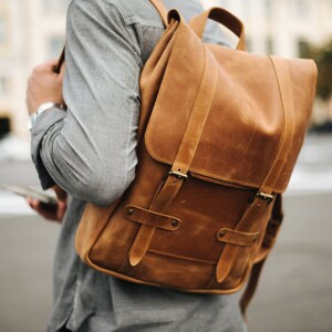 May include: A brown leather backpack with two adjustable straps and buckles. The backpack has a flap with a buckle closure.