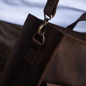 May include: A brown leather satchel bag with a strap and a metal clasp. The bag has a flap with a buckle closure and a pocket on the front.