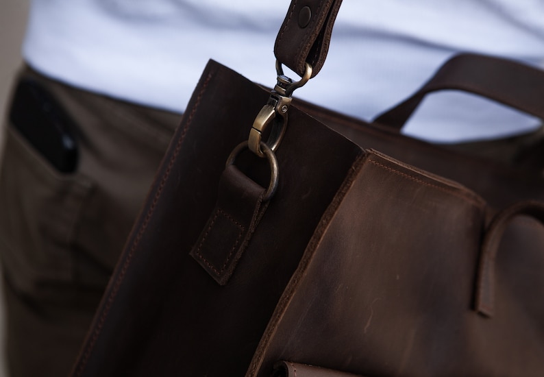May include: A brown leather satchel bag with a strap and a metal clasp. The bag has a flap with a buckle closure and a pocket on the front.