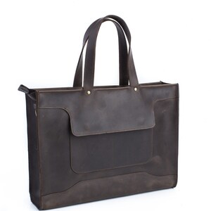K&ouml;nnte beinhalten: Eine braune Ledertasche mit einer gro&szlig;en Fronttasche und zwei Henkeln oben.