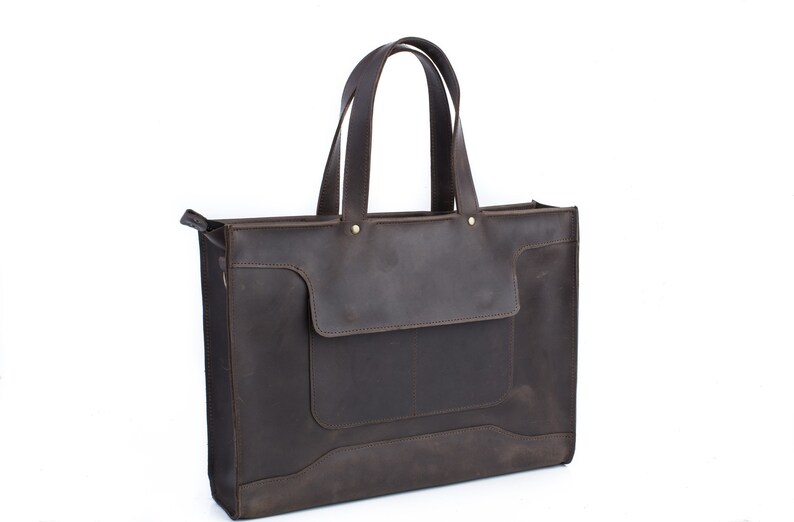 K&ouml;nnte beinhalten: Eine braune Ledertasche mit einer gro&szlig;en Fronttasche und zwei Henkeln oben.