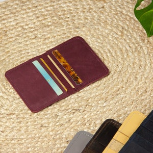 May include: A burgundy leather wallet with multiple card slots, open to reveal several cards inside. The wallet is lying on a woven straw mat.