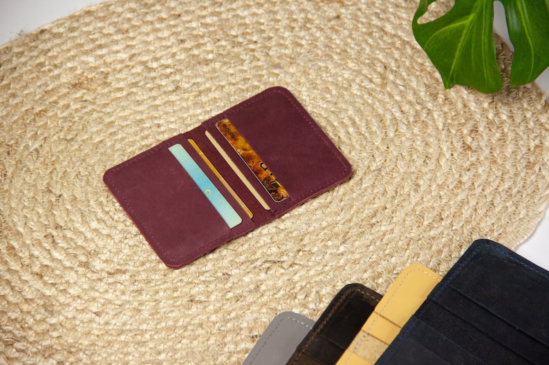 May include: A burgundy leather wallet with multiple card slots, open to reveal several cards inside. The wallet is lying on a woven straw mat.