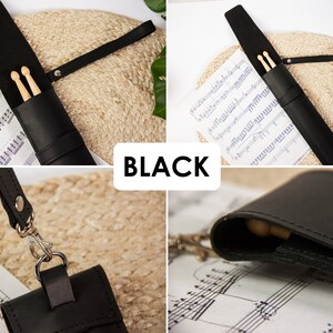May include: Black leather drumstick holder with a strap and a snap closure. The holder is lying on a sheet of music.