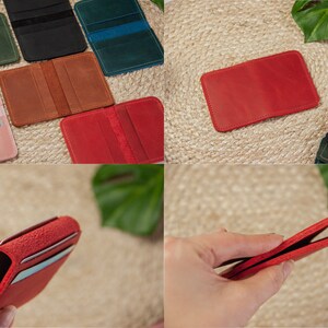 May include: A set of six leather card holders in various colors, including pink, red, brown, green, and black. The card holders are laid out on a woven surface and a hand is holding one of the red card holders open.