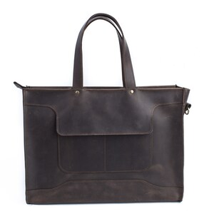 K&ouml;nnte beinhalten: Eine braune Ledertasche mit Rei&szlig;verschluss und einer Fronttasche. Die Tasche hat zwei obere Tragegriffe und einen abnehmbaren Schultergurt.