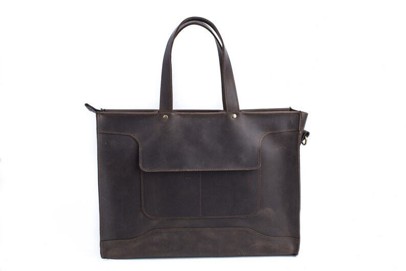 K&ouml;nnte beinhalten: Eine braune Ledertasche mit Rei&szlig;verschluss und einer Fronttasche. Die Tasche hat zwei obere Tragegriffe und einen abnehmbaren Schultergurt.