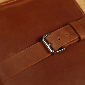 May include: A brown leather journal with a brown leather strap and a silver buckle.