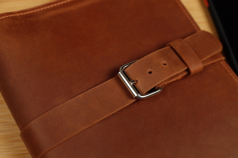 May include: A brown leather journal with a brown leather strap and a silver buckle.