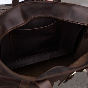 May include: A brown leather tote bag with a zippered top and a smaller pocket inside. The bag has two straps and a buckle on the front.