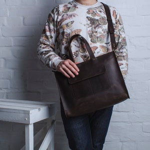 K&ouml;nnte beinhalten: Eine braune Ledertasche mit einem oberen Henkel und einem Schultergurt. Die Tasche hat eine Fronttasche und ist aus strukturiertem Leder gefertigt.