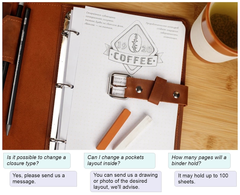 May include: A brown leather binder with a metal ring closure and a leather strap. The binder has a white page with a drawing of a coffee cup and the text "1920 COFFEE". The binder is on a wooden surface with a cup of tea and two colored pencils.