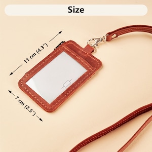 Puede incluir: Un porta-credencial de cuero marrón con una ventana de plástico transparente. El porta-credencial está unido a un cordón de cuero marrón. El porta-credencial mide 7 cm (2,5 pulgadas) por 11 cm (4,3 pulgadas).