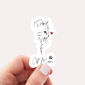 May include: A white sticker with a black line drawing of a cat's head with a red heart. The text "Cat Mom" is written below the cat with a black paw print.