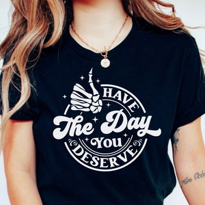 May include: A black t-shirt with a white graphic that says "Have the Day You Deserve" with a skeleton hand giving a thumbs up.