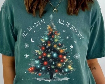May include: A teal blue t-shirt with a Christmas tree graphic and the text "All is Calm, All is Bright".
