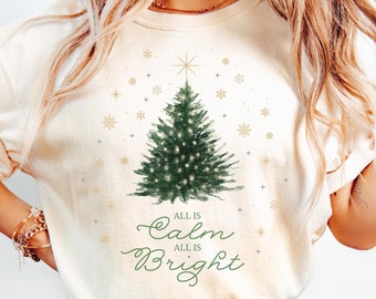 May include: Ivory t-shirt with a watercolor illustration of a Christmas tree with lights and the text "All is Calm All is Bright".