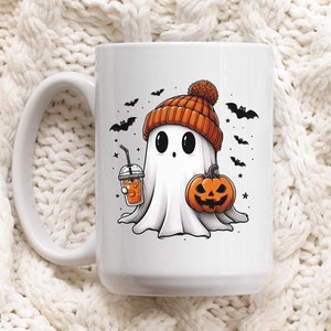 May include: White ceramic mug with a Halloween-themed design. A cartoon ghost wearing an orange and white hat holds a pumpkin and a cup of orange liquid. The ghost has large black eyes and a small mouth. Bats and stars are in the background.