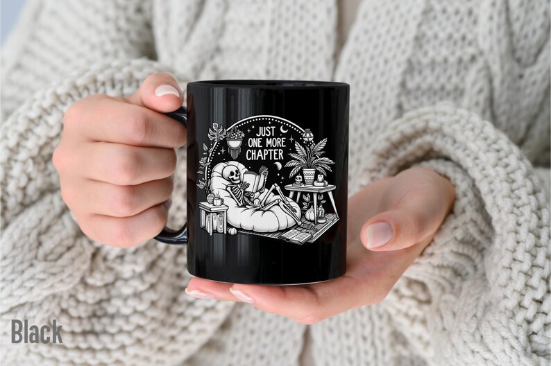 Black coffee mug with skeleton reading while lounging in a boho style room with the words Just One More Chapter