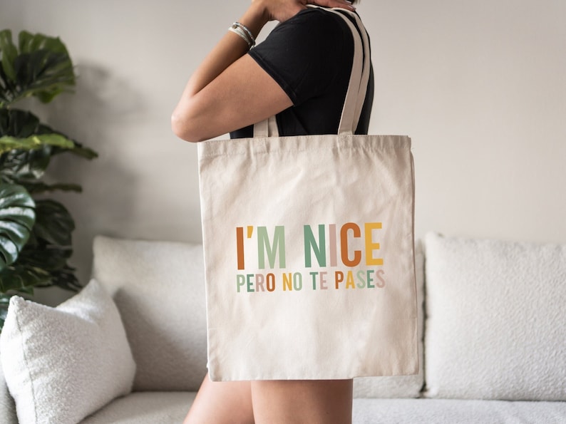 May include: A white canvas tote bag with the text "I'M NICE PERO NO TE PASES" in colorful letters. The text is in a rainbow color scheme.