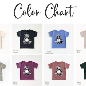 May include: Color chart showing ten different t-shirt colors with a black and white illustration of a raccoon wearing a mask and holding a candy bag. The colors are Natural, Dark Gray Heather, Heather Columbia Blue, Heather Dust, Heather Stone, Heather Maroon, Heather Mauve, Forest Green.