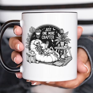 Black and white coffee mug with skeleton reading while lounging in a boho style room with the words Just One More Chapter