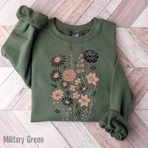 Op de afbeelding: Militairgroen sweatshirt met een bloemenontwerp in zwart en perzik. De crew neck sweatshirt heeft lange mouwen met geribde manchetten. De tekst "Military Green" staat onderaan de afbeelding.