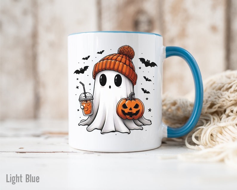 May include: White ceramic mug with a light blue rim and handle. The mug features a cartoon ghost wearing an orange knit hat and holding a pumpkin and a cup of orange liquid. The background includes black bats and stars.