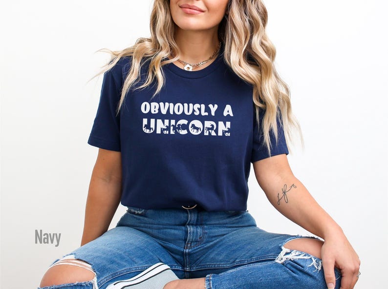 May include: A navy blue t-shirt with the text "OBVIOUSLY A UNICORN" in white. The word "UNICORN" is made up of a series of small white unicorn silhouettes.