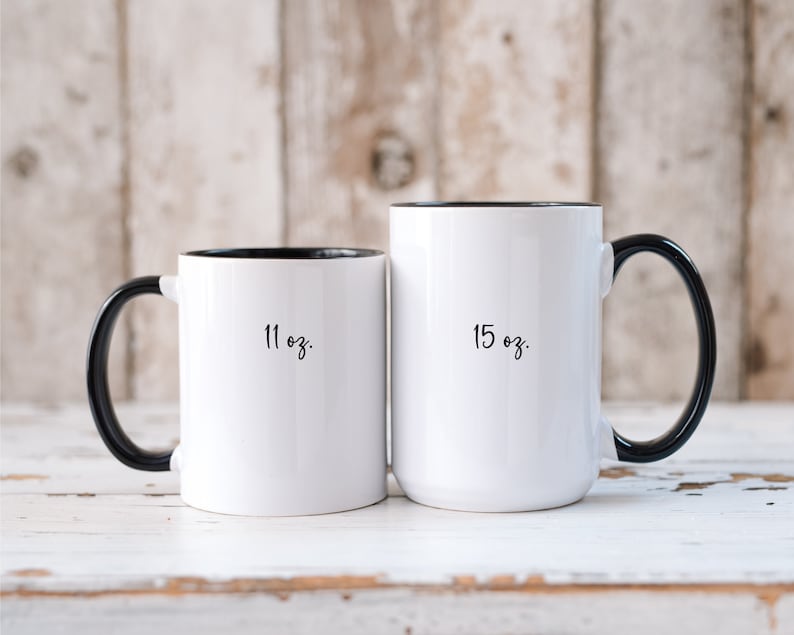 May include: Two white ceramic mugs with black handles and black rims. The mug on the left is 11 oz and the mug on the right is 15 oz.