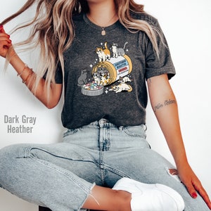 May include: Dark gray heather t-shirt with a graphic of a pill bottle overflowing with cats and the text "Serotonin Booster" on the label.