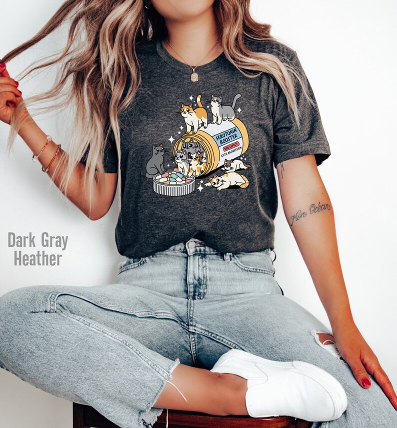 May include: Dark gray heather t-shirt with a graphic of a pill bottle overflowing with cats and the text "Serotonin Booster" on the label.