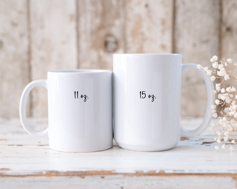 Op de afbeelding: Twee witte keramische mokken met zwarte letters. De kleinere mok is 11 oz en de grotere mok is 15 oz.