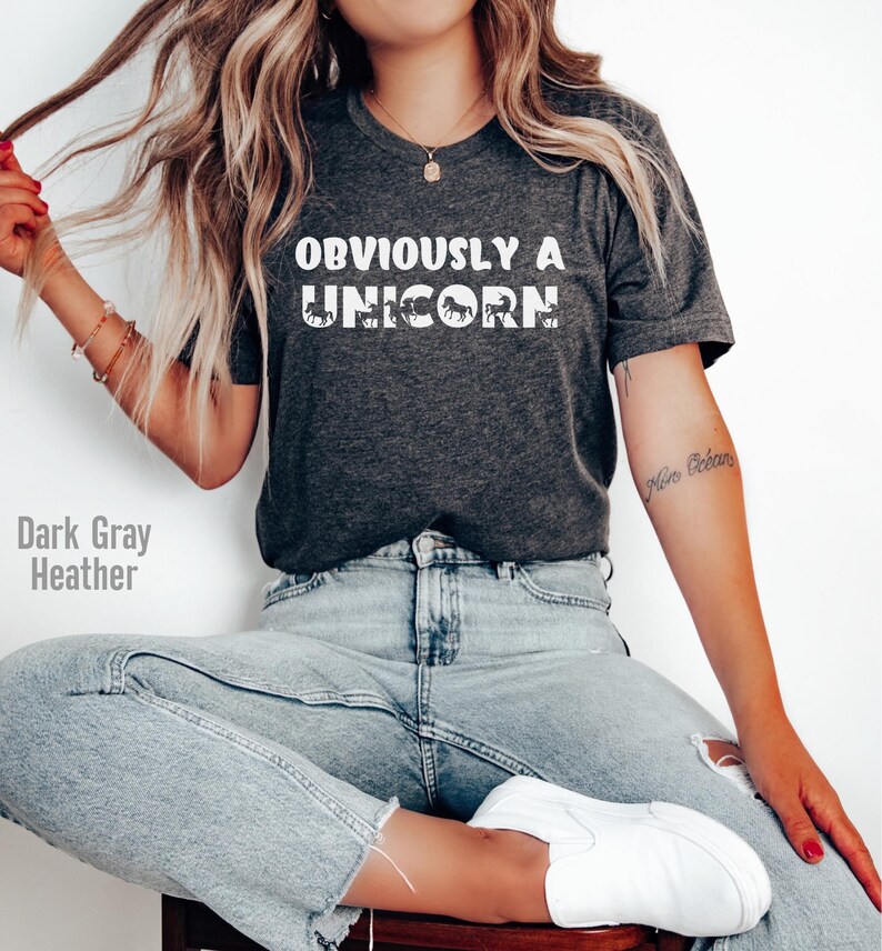 May include: A dark gray heather t-shirt with the text "OBVIOUSLY A UNICORN" in white. The shirt features a graphic of a unicorn with a rainbow mane.